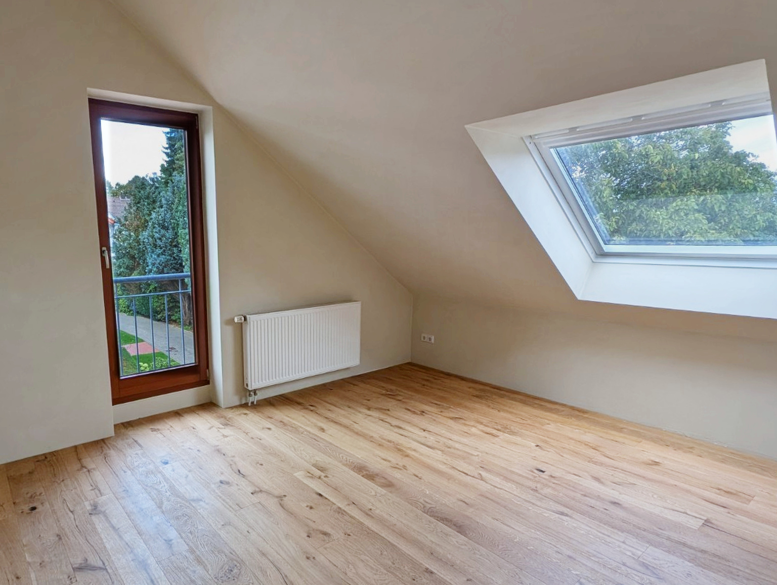 Dachzimmer nach den Arbeiten mit hellen Wandflächen und Holzboden, Blick auf Balkontür und Dachfenster