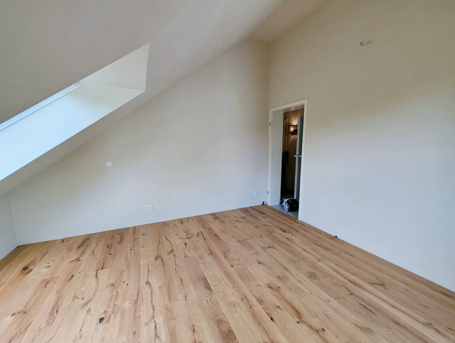 Dachzimmer nach den Arbeiten mit überarbeiteten Wandflächen und Holzboden, Blick zur Zimmertür