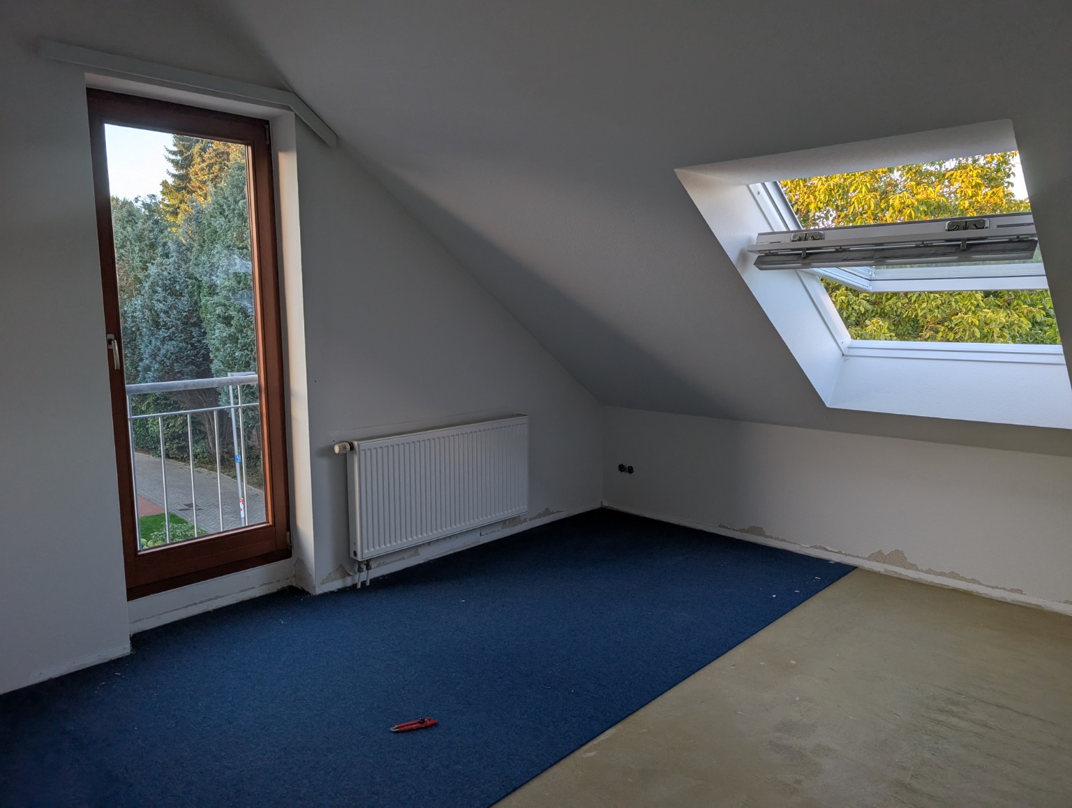 Dachzimmer vor den Arbeiten mit teils entferntem Bodenbelag, Blick auf Balkontür und Dachfenster